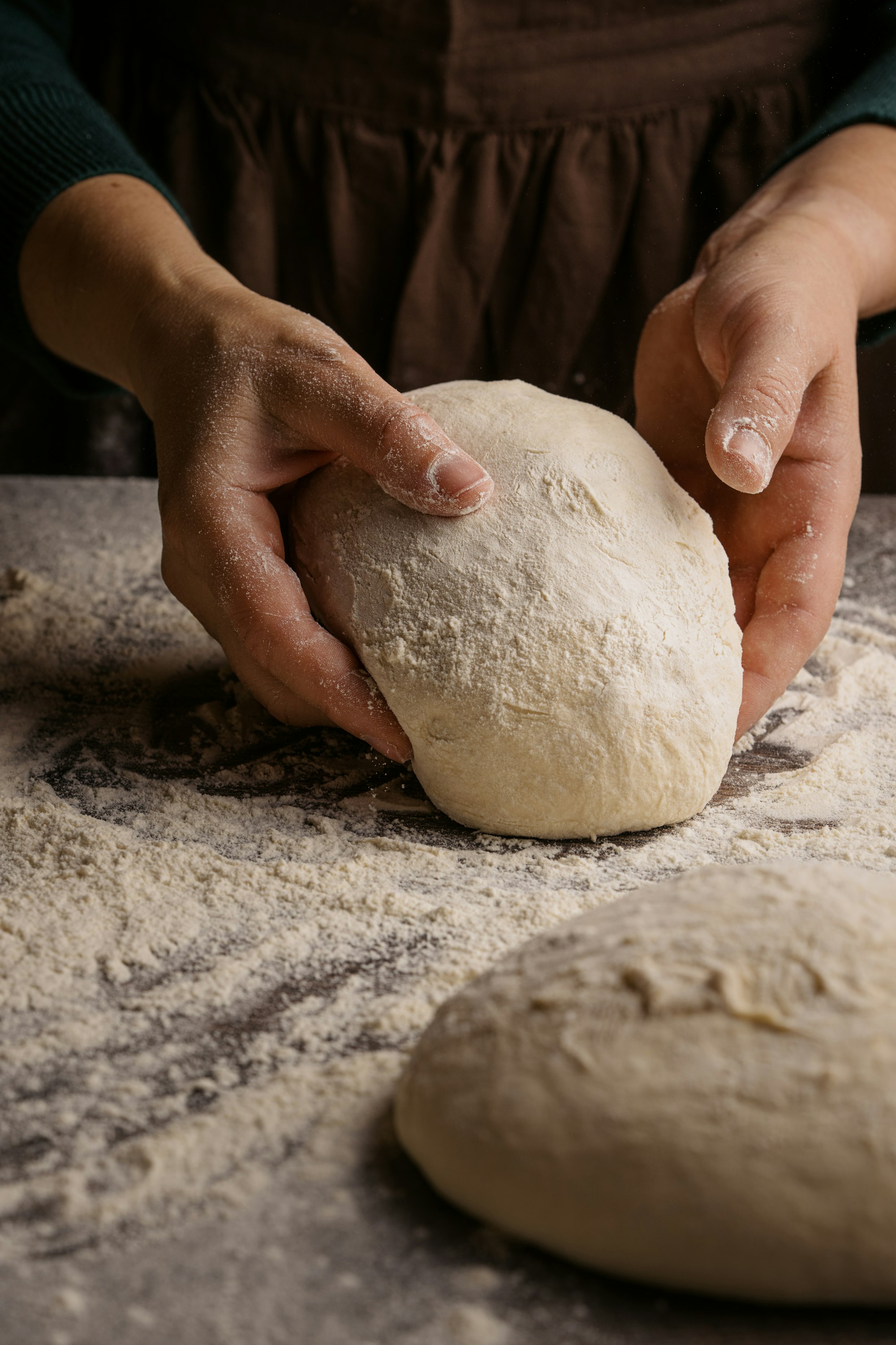Hands shaping a ball of dough on a floured counter