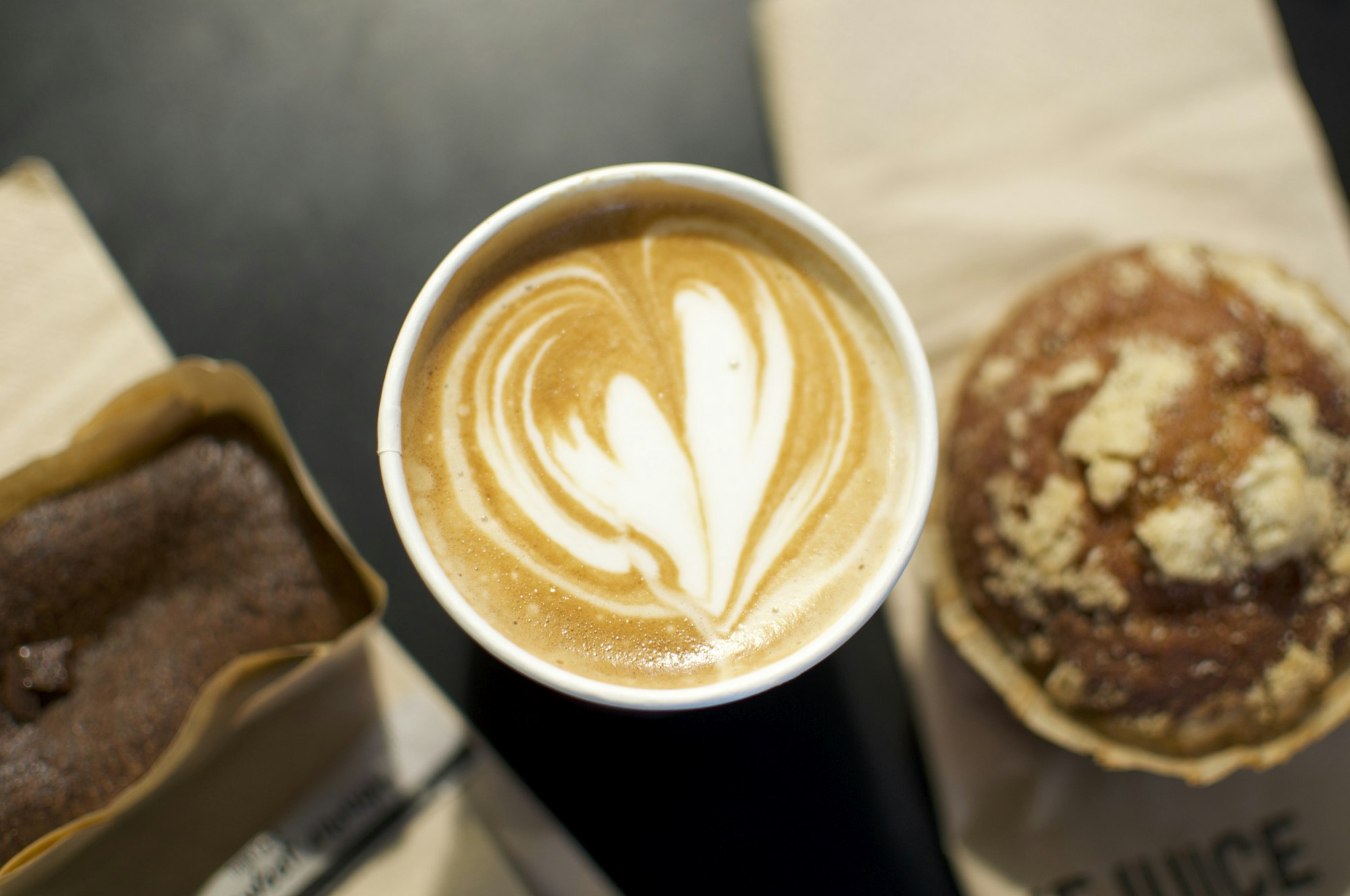 A latte with heart art beside a pastry